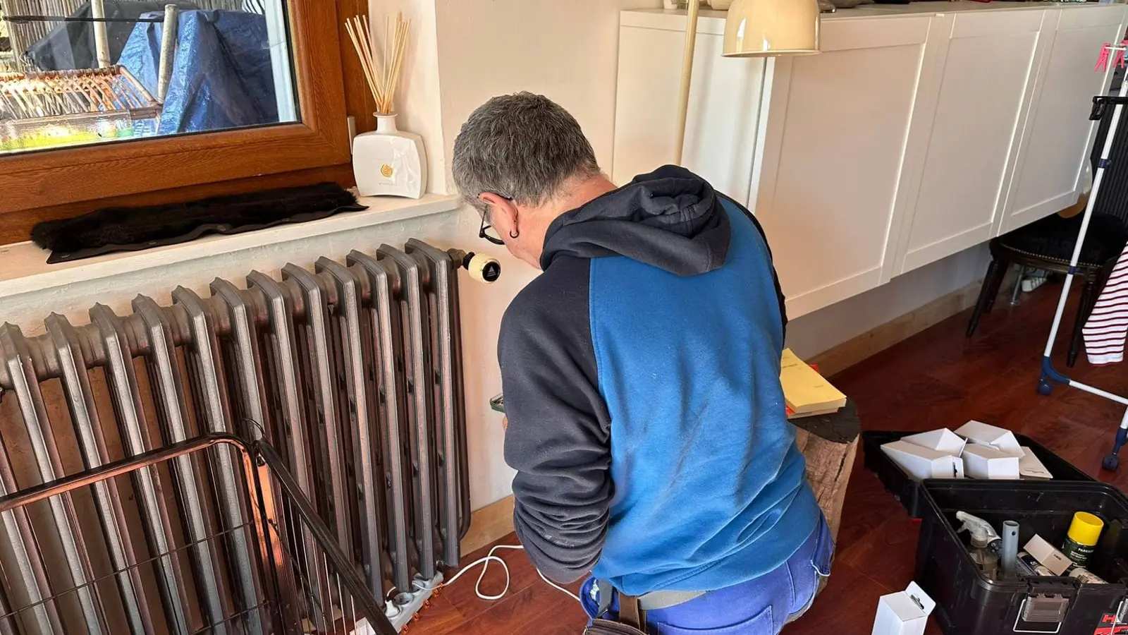 Technicien installant une tête thermostatique connectée sur un radiateur en fonte, dans un logement occupé